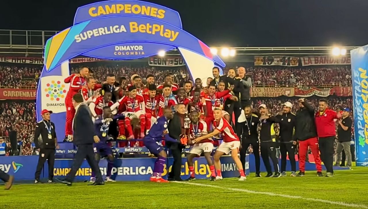 El capitán Hugo Rodallega levanta el trofeo de la Superliga 2026 en el centro del estadio El Campín, rodeado por la plantilla y el cuerpo técnico, celebrando el quinto título de Santa Fe en la historia de este torneo. Foto: Captura video